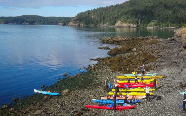 A group of colorful kayaks rest on a rocky shore beside a blue body of water